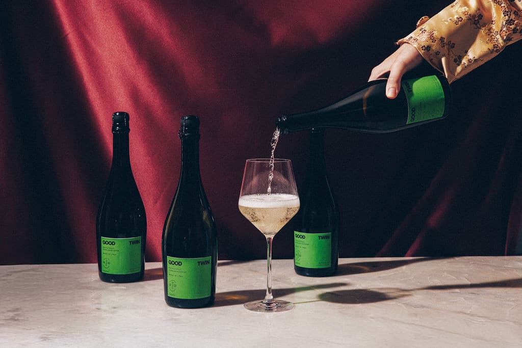 A hand pouring a bottle of Good Twin into a glass on a marble table