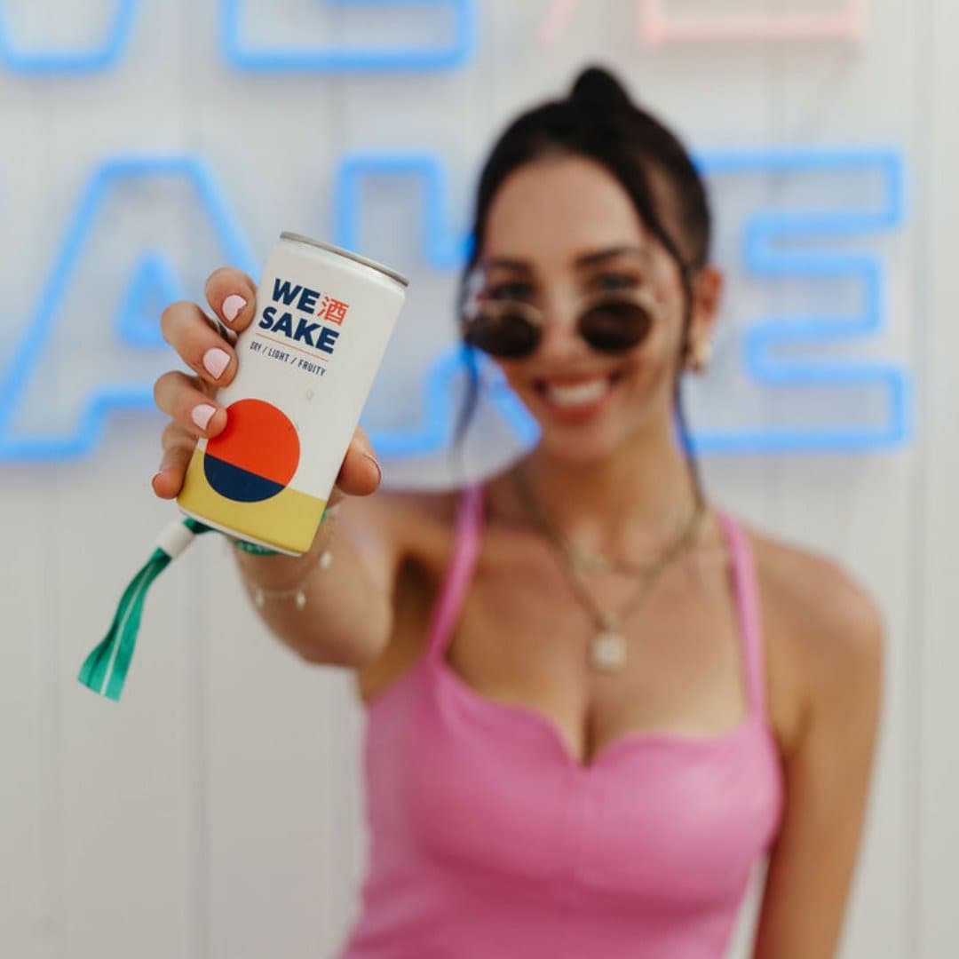 A woman holding a can of WESAKE in front of an illuminated WESAKE sign